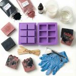 Aktif karbon ve gül tozu ile sabun yapımı için kullanılan malzemeler, silikon sabun kalıpları, eldiven, karıştırıcılar ve elde yapılmış sabunlar bulunan çalışma alanı