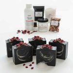 Aktif karbonlu çay ağacı yağlı el yapımı siyah sabunlar ve arka planda sabun yapım malzemeleri ahşap sunum tahtası üzerinde