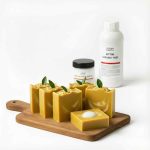 Ahşap tahtada sergilenen el yapımı sarı bıttım sabunları ve arka planda bıttım sabunu yağı ile kostik kabı